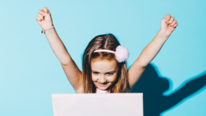 Girl in front of laptop with arms in the air cheering